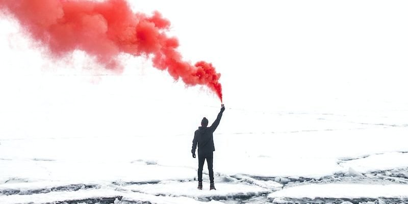 selective color photography of person holding orange gas smoke standing on snow